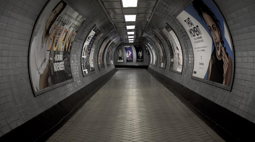 地铁跑酷直接进入的通勤人群场景，地铁站台上多人低头看手机，暖橙色灯光与橄榄绿墙面形成柔和对比